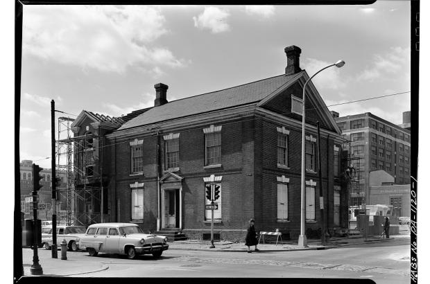 Black and white photo of two-story brick building with a car in front