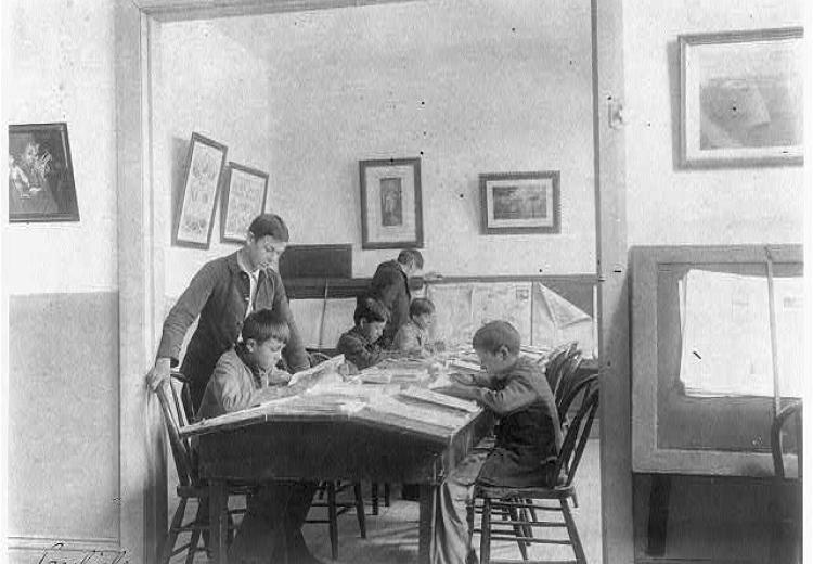 Four young boys sitting around a table covered in newspapers. Two older boys stand next to them.